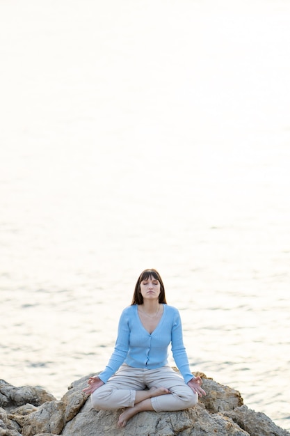 Caucasian woman meditating in front of the sea in casual clothes