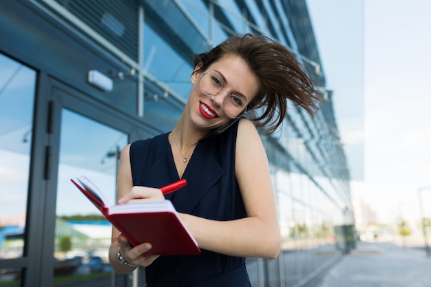 Caucasian woman in office clothes writes to notebook near the office building