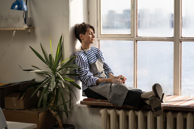 Caucasian woman potter enjoy drinking hot tea from handicraft mug in creative studio of ceramic art