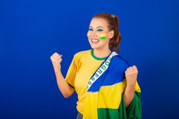 Caucasian woman redhead Brazil soccer fan Brazilian blue background wearing flag of Brazil celebrating