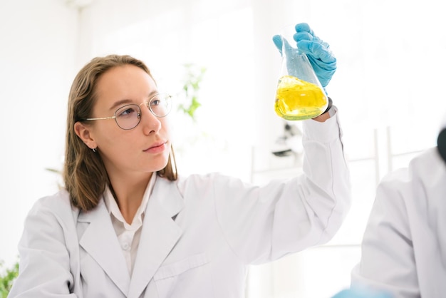 Caucasian woman scientist researcher wearing eye glasses shaking substance in the conical flask for analysis of liquids in the lab Scientist working with a dropper and the conical flask