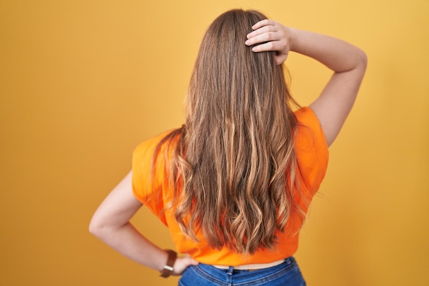 Caucasian woman standing over yellow background backwards thinking about doubt with hand on head