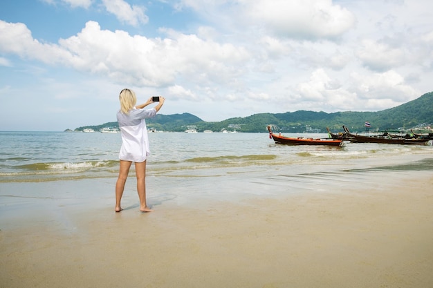 Caucasian woman traveler in white dress makes selfie photo with sea view summer travel vacation concept