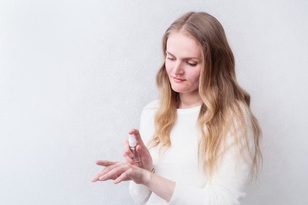 Caucasian woman uses hand sanitizer on the light background with copy space