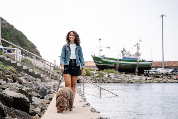 Photo caucasian woman walking her water dog across the harbor walk. horizontal view of woman traveling with animal. animals and travel concept.