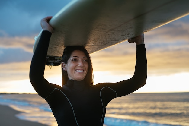 Caucasian woman wearing a surfing suit with a surfboard happily smiling