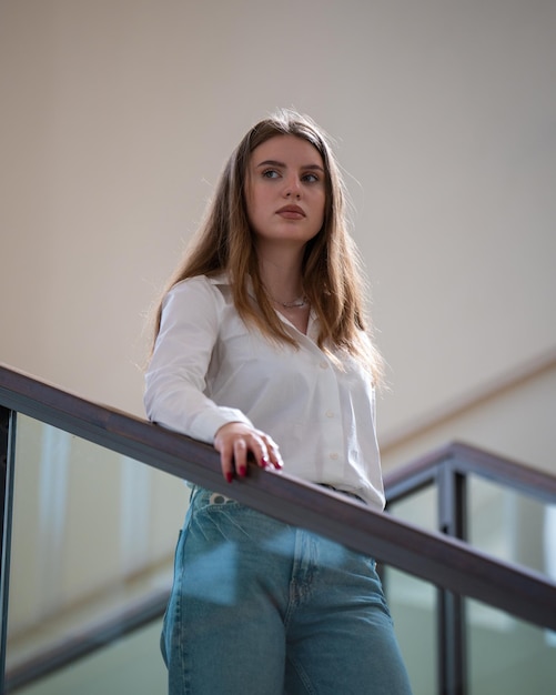 Caucasian young cute woman going down the stairs A brunette student with long hair in a white blouse visits the library