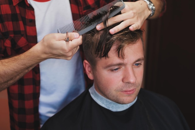 Caucasian young man in Barbershop Barber is cuttinhg his hair in hipster style