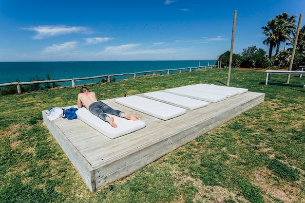 Caucasian young man shirtless and in jeans lying down on the beach 