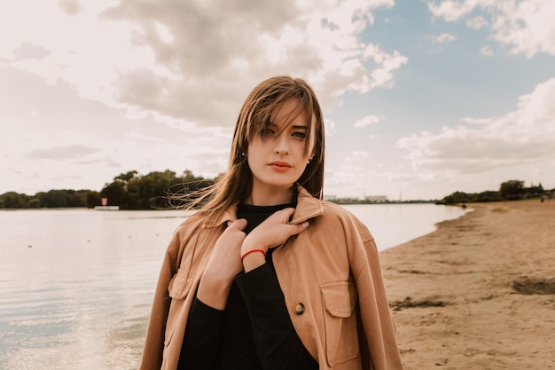 Caucasian young pretty stylish woman standing near river lake water street on sand pier