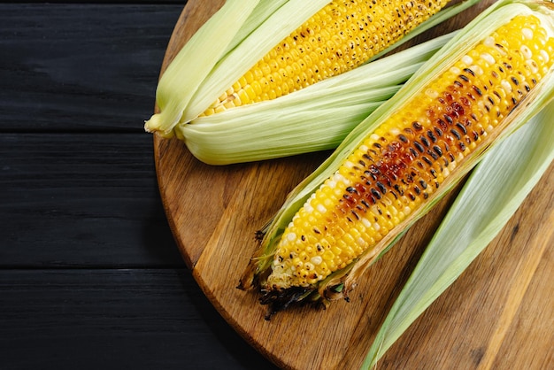 A cauldron of corn roasted over charcoal on a wooden board whole corn cobs