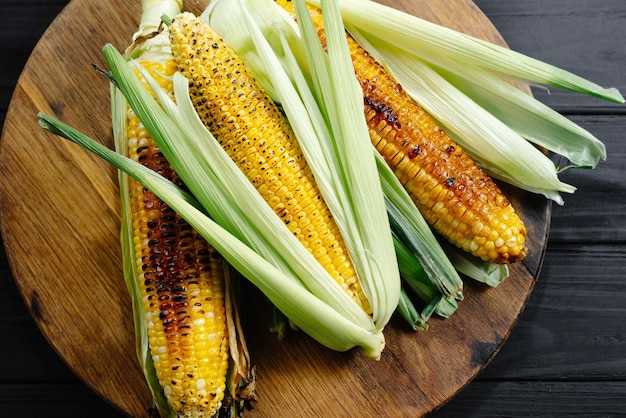 A cauldron of corn roasted over charcoal on a wooden board whole corn cobs