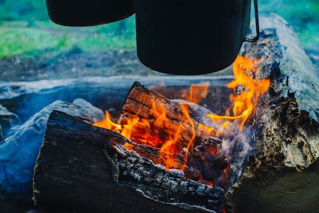 Cauldron and kettle above bonfire. Cooking of food on nature. Dinner outdoors. Firewood and branches in fire. Active rest. Camping in forest.