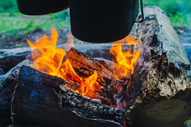 Cauldron and kettle above bonfire. Cooking of food on nature. Dinner outdoors. Firewood and branches in fire. Active rest. Camping in forest.