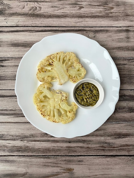 Cauliflower steaks with pesto sauce on a white plate on a wooden plate top view vertical arrangement