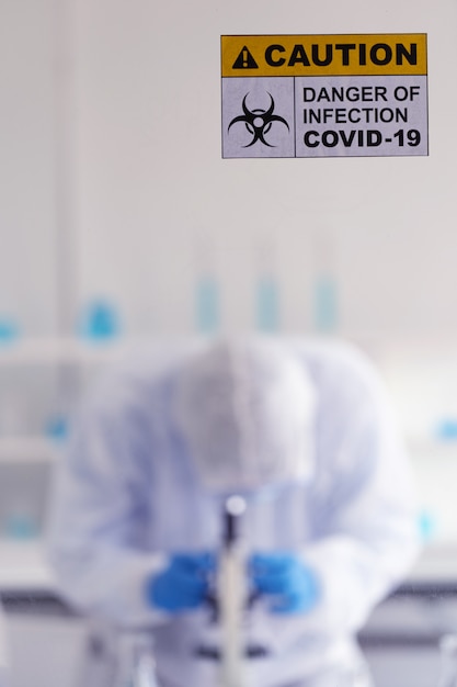 Caution danger Signage of COVID-19 coronavirus in front of Laboratory room with background of Scientists working and researching vaccine for ncov-19 virus for world pandemic situation.