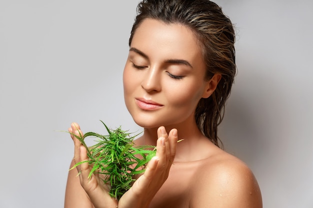 CBD cosmetics concept. Beautiful woman with a cannabis leaf on gray background