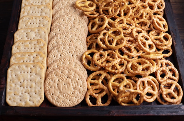 Cclose-up of wooden box with cookies, crackers and mini salted pretzels, party snacks.