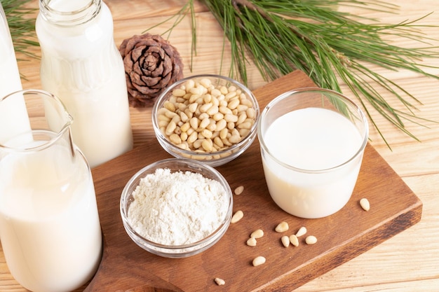 Cedar nut products Glass and bottles with milk nuts and powder on wooden table Selective focus