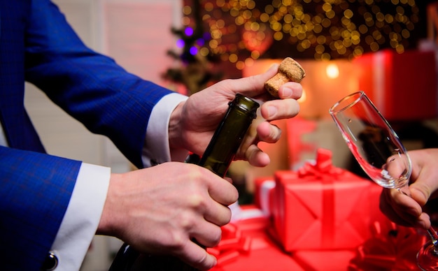 Celebrate new year with champagne Hands opening champagne bottle and hold glass christmas decorations background Cheers concept Last minute before new year Drink champagne or sparkling wine