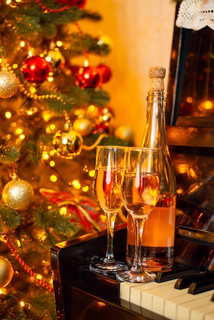 Celebrating Christmas with champagne Two glasses of champagne or wine and bottle on piano near decorated christmas tree all in bright lights