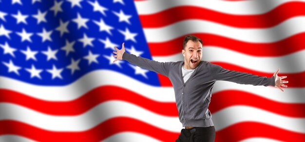 Celebrating an Independence day. Stars and Stripes. Young man with the flag of the United States of America isolated on white studio background. Looks crazy happy and proud as a patriot of his country