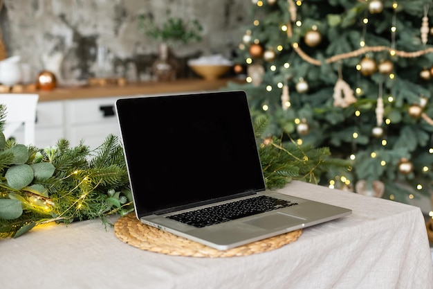 Celebrating merry christmas and new year at home, candles and garlands, laptop on the table in the kitchen.