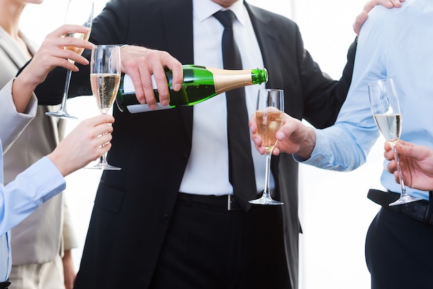 Celebrating success together. Close-up of business people holding flutes while man pouring champagne