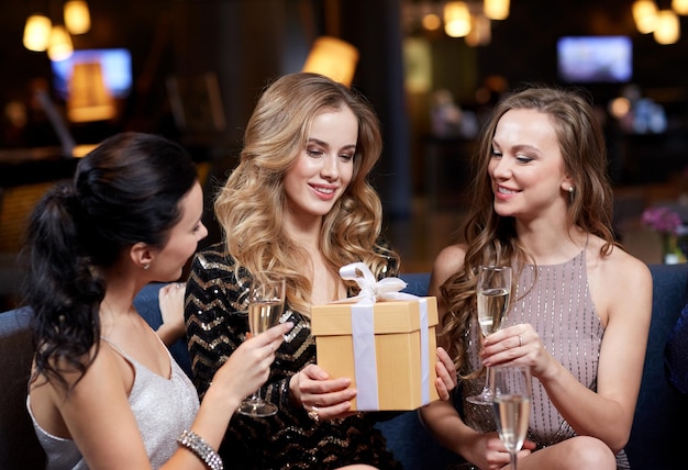 celebration, friends, bachelorette party, birthday and holidays concept - happy women with champagne glasses and gift box at night club