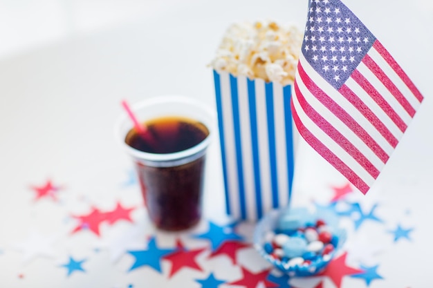 celebration, patriotism and holidays concept - close up of american flag, coca cola cup, popcorn and candies with stars confetti decoration at 4th july party on independence day