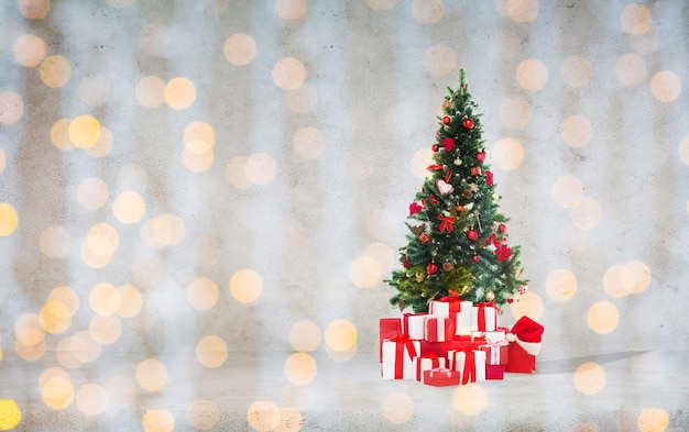 celebration, winter holidays and advertisement concept - christmas tree with gifts and santa hat over concrete wall background