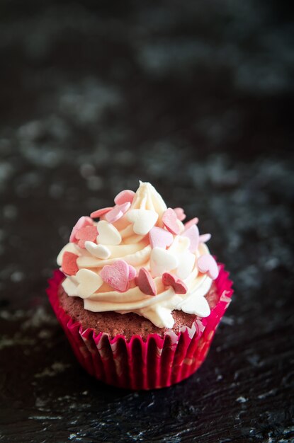 Celebratory cupcake for Valentines day on wooden black table with hearts.