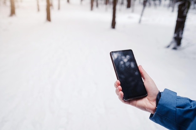 Cell phone in a man's hand against a beautiful snowy winter forest background