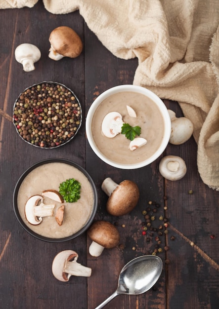 Ceramic bowl plates of creamy chestnut champignon mushroom soup with spoon pepper and kitchen cloth on dark wooden board