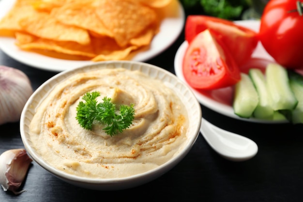 Ceramic bowl of tasty hummus with chips and parsley on table