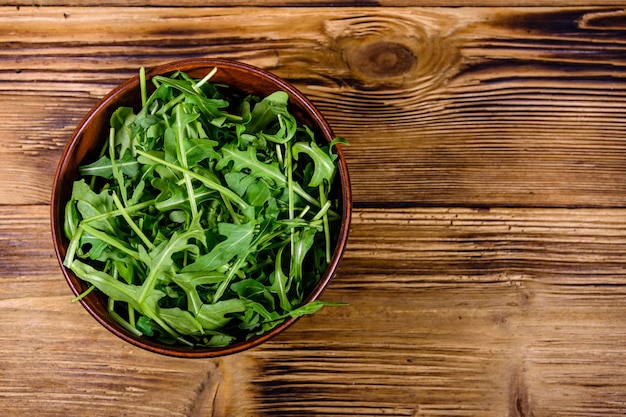 Ceramic bowl with arugula leaves on a wooden table. Top view