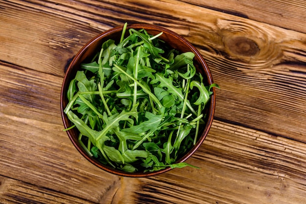 Ceramic bowl with arugula leaves on a wooden table Top view