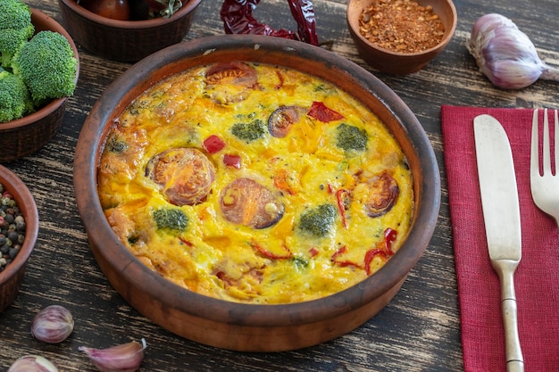 Ceramic bowl with vegetable frittata simple vegetarian food Frittata with egg tomato pepper onion broccoli and cheese on wooden table Italian egg omelette