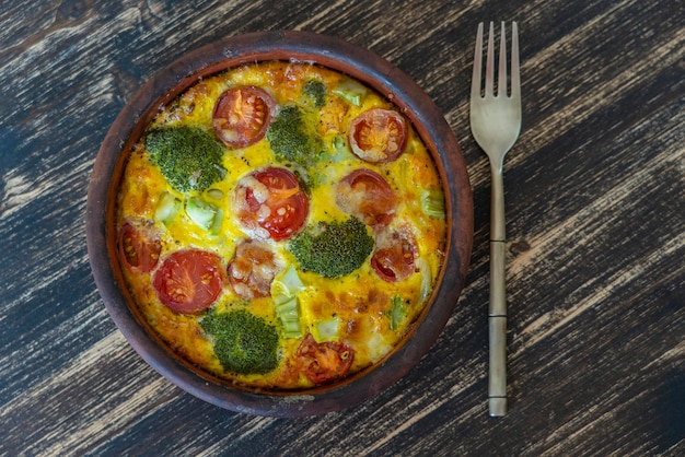 Ceramic bowl with vegetable frittata simple vegetarian food Frittata with egg tomato pepper onion broccoli and cheese on wooden table Italian egg omelette