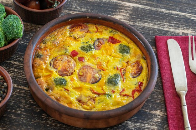 Ceramic bowl with vegetable frittata simple vegetarian food Frittata with egg tomato pepper onion broccoli and cheese on wooden table Italian egg omelette