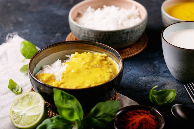 Ceramic bowl of yellow curry served with basil and limes