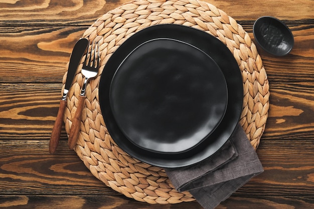 Ceramic empty black plate silverware and linen kitchen towel napkin on old brawn wooden table background Cooking stone backdrop Top view with copy space Flat lay