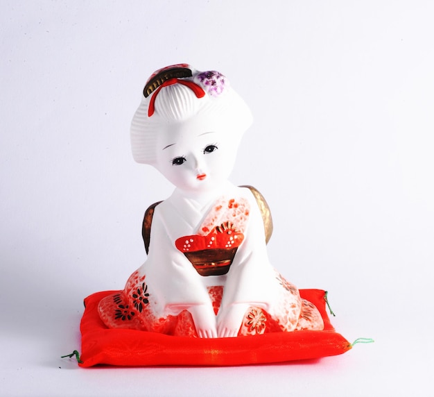 Photo ceramic japanese female doll dressed in kimono sitting on bright orange pillow