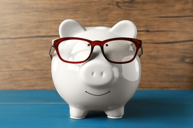 Ceramic piggy bank with glasses on blue wooden table