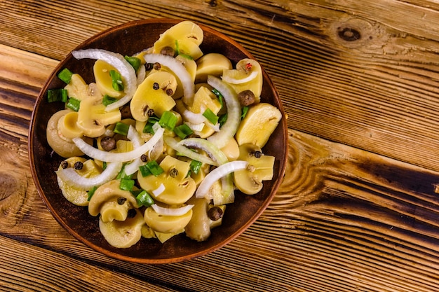 Ceramic plate with canned mushrooms on wooden table Top view