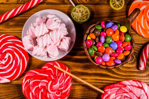 Ceramic plate with marshmallow candy cane and lollipops on a wooden table Top view