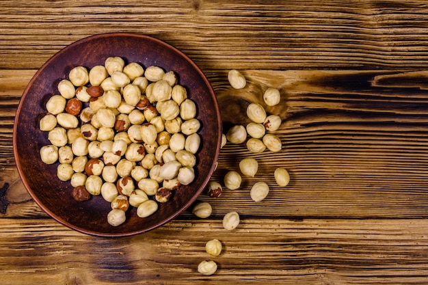 Ceramic plate with peeled hazelnuts on a wooden table. Top view