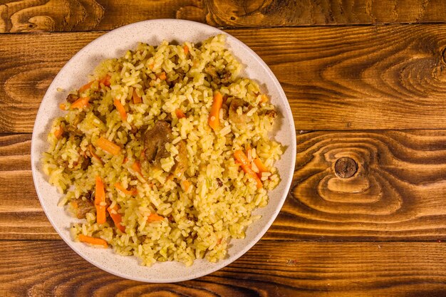 Ceramic plate with pilaf on rustic wooden table. Top view