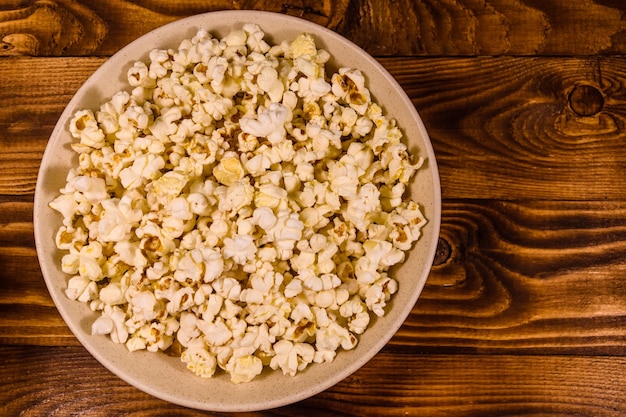 Ceramic plate with popcorn on wooden table Top view