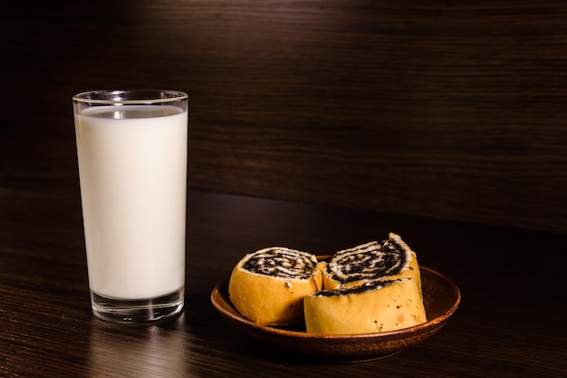 Ceramic plate with poppy seed buns and a glass of milk on dark wooden table